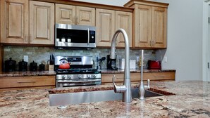 A kitchen with wooden cabinets, a stainless steel microwave, a gas stove, and a modern sink with a high-arc faucet. - Walk To Beach | Heated Lagoon Pool, on Anna Maria! (Holmes Beach)