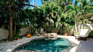 Ein Swimmingpool, umgeben von tropischer Vegetation und einem weißen Liegestuhl.