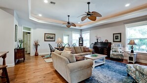 A spacious living room with hardwood flooring, a beige sofa, a coffee table, and a piano. - Walk To Beach | Heated Lagoon Pool, on Anna Maria! (Holmes Beach)