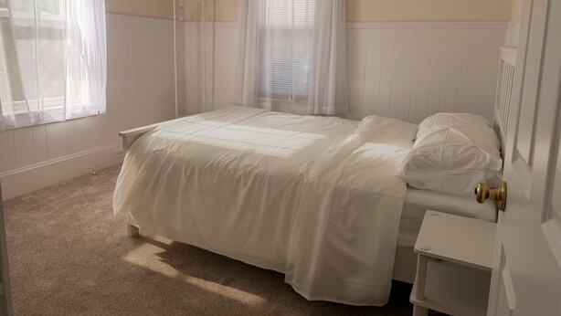 A bedroom with a bed, a nightstand, a window with curtains, and a radiator.