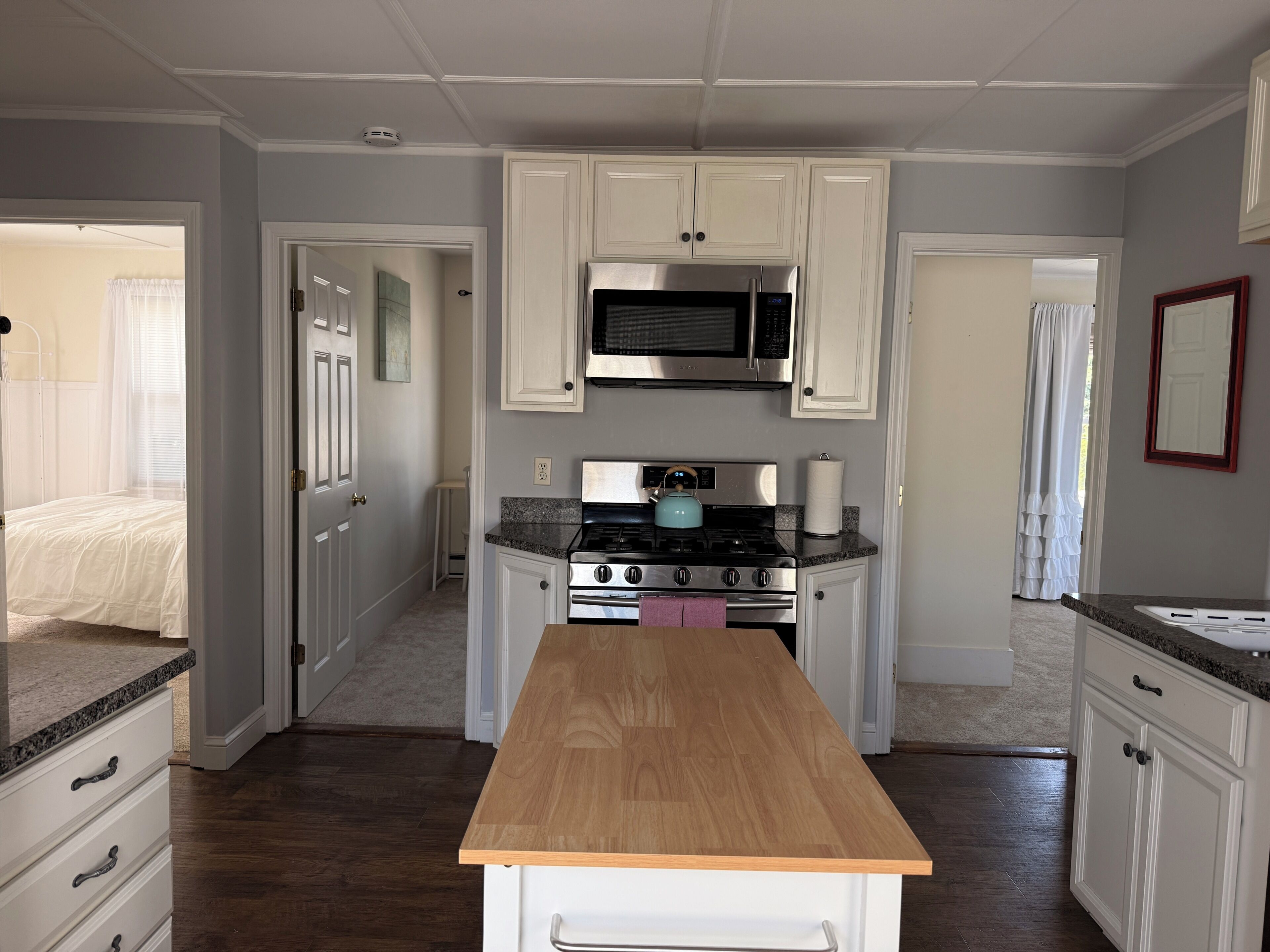 A kitchen with white cabinets, a stainless steel microwave, a gas stove, and a wooden countertop.