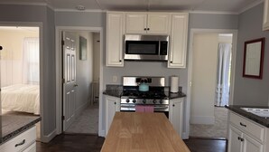 A kitchen with white cabinets, a stainless steel microwave, a gas stove, and a wooden countertop.