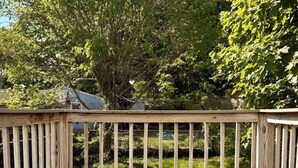 A wooden deck with a railing, surrounded by greenery and trees.