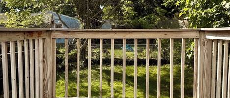 A wooden deck with a railing, surrounded by greenery and trees.