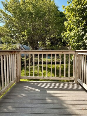 A wooden deck with a railing, surrounded by greenery and trees.