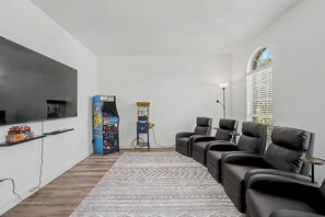 Un salon équipé d’un téléviseur à écran plat, de jeux d’arcade, d’un fauteuil massant et d’un tapis à motifs.