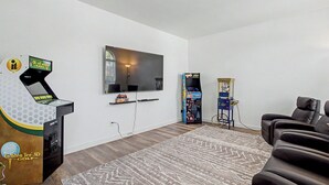 A living room with a flat-screen TV, a golf arcade game, and a claw machine. - Family Reunion HQ, Sleeps 14 Frisco, Hot Tub (Frisco)