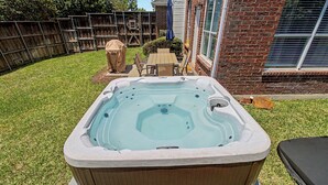 A hot tub in a backyard with a wooden deck, a brick house, and a covered patio table. - Family Reunion HQ, Sleeps 14 Frisco, Hot Tub (Frisco)