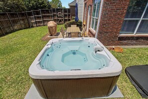 Ein Whirlpool in einem Garten mit einer Holzterrasse, einem Ziegelhaus und einem überdachten Patio-Tisch.