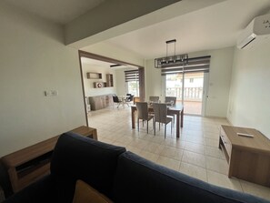 Ein geräumiger Wohnbereich mit einer Couch, einem Esstisch mit Stühlen und einer Küchenzeile im Hintergrund.