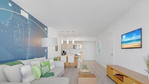 A modern living room with a large wall map, a sofa with cushions, a dining area, and a kitchen in the background. - New! Sunset Suite 2BR - Bay View Fitness Center (Hallandale Beach)