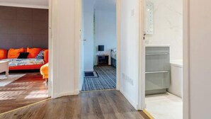 Um interior moderno com piso de madeira, um sofá com almofadas laranja e um banheiro visível com espelho e espaço de armazenamento.