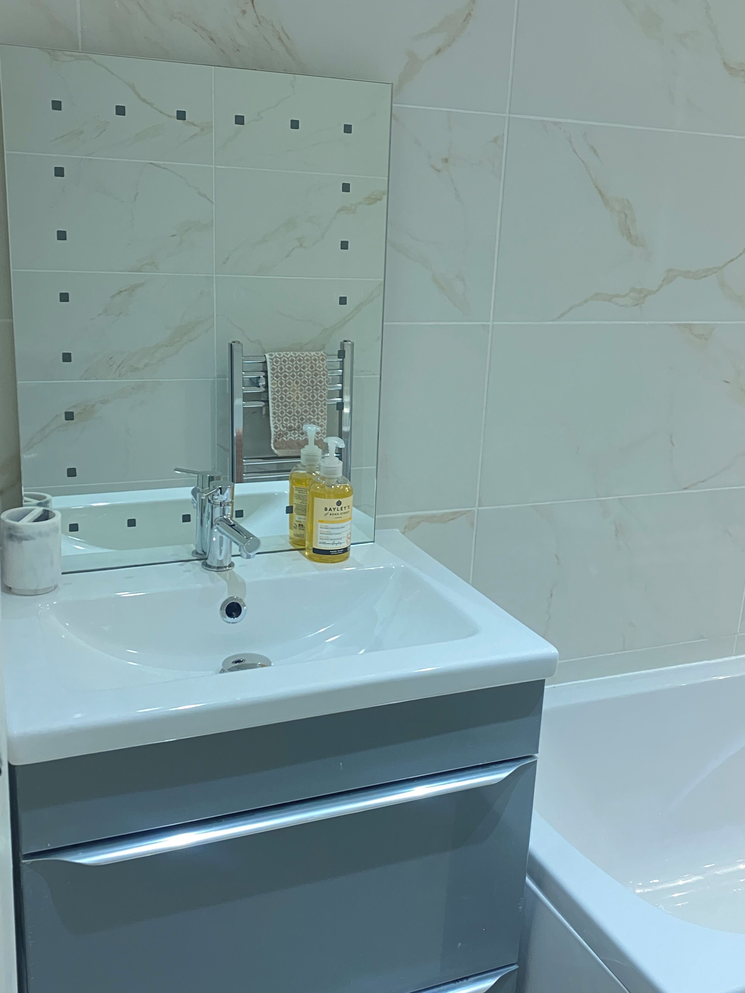 Ein Badezimmer mit einem weißen Waschbecken, einem Spiegel, einem Handtuchhalter und einer Seife.