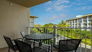 Uma varanda com uma mesa redonda e quatro cadeiras, com vista para uma paisagem verdejante e um edifício de hotel.