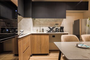 A modern kitchen with wooden cabinets, a built-in oven, a coffee maker, and a dining area with a table. - Modern 2BR Providencia Oasis with Pool  (Santiago)
