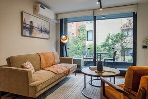A modern living room with a sofa, a coffee table, and a view of the city through large windows. - Modern 2BR Providencia Oasis with Pool  (Santiago)