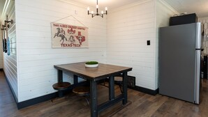 A kitchen with a wooden table, two stools, a refrigerator, and a wall-mounted sign.