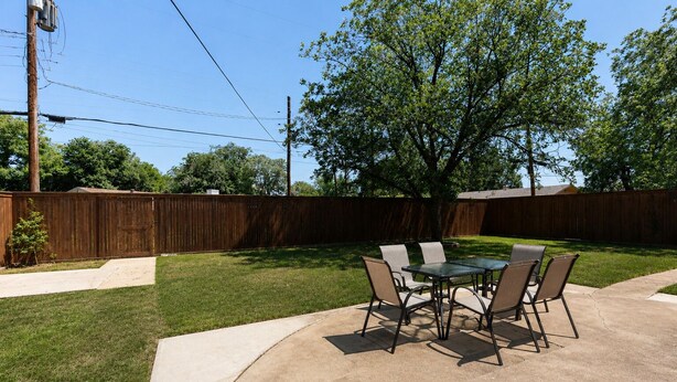 A backyard patio with a table and chairs, surrounded by a wooden fence and a tree.
