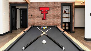 A pool table with a T-shaped sign on the wall, a billiards cue, and a set of balls.