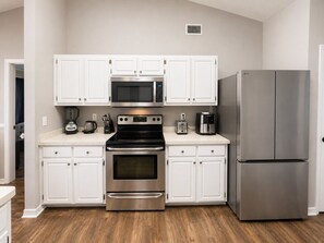 A modern kitchen with white cabinets, stainless steel appliances including a microwave, oven, and refrigerator, and a wooden floor. - Ortega Oasis- New Listing in Navarre, 10 minutes to Navarre Beach! (Navarre)