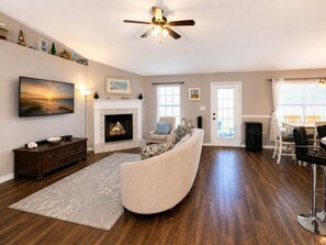 A living room with a fireplace, a sofa, a television, and a dining area with chairs. - Ortega Oasis- New Listing in Navarre, 10 minutes to Navarre Beach! (Navarre)