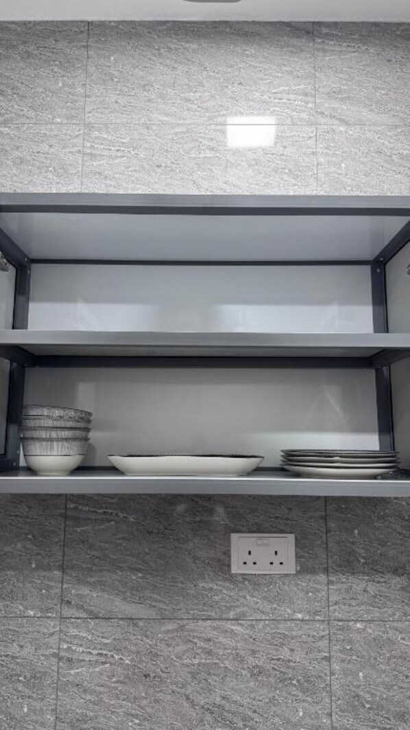A kitchen with grey marble tiles, a black-framed shelf with bowls and plates, and a power outlet.