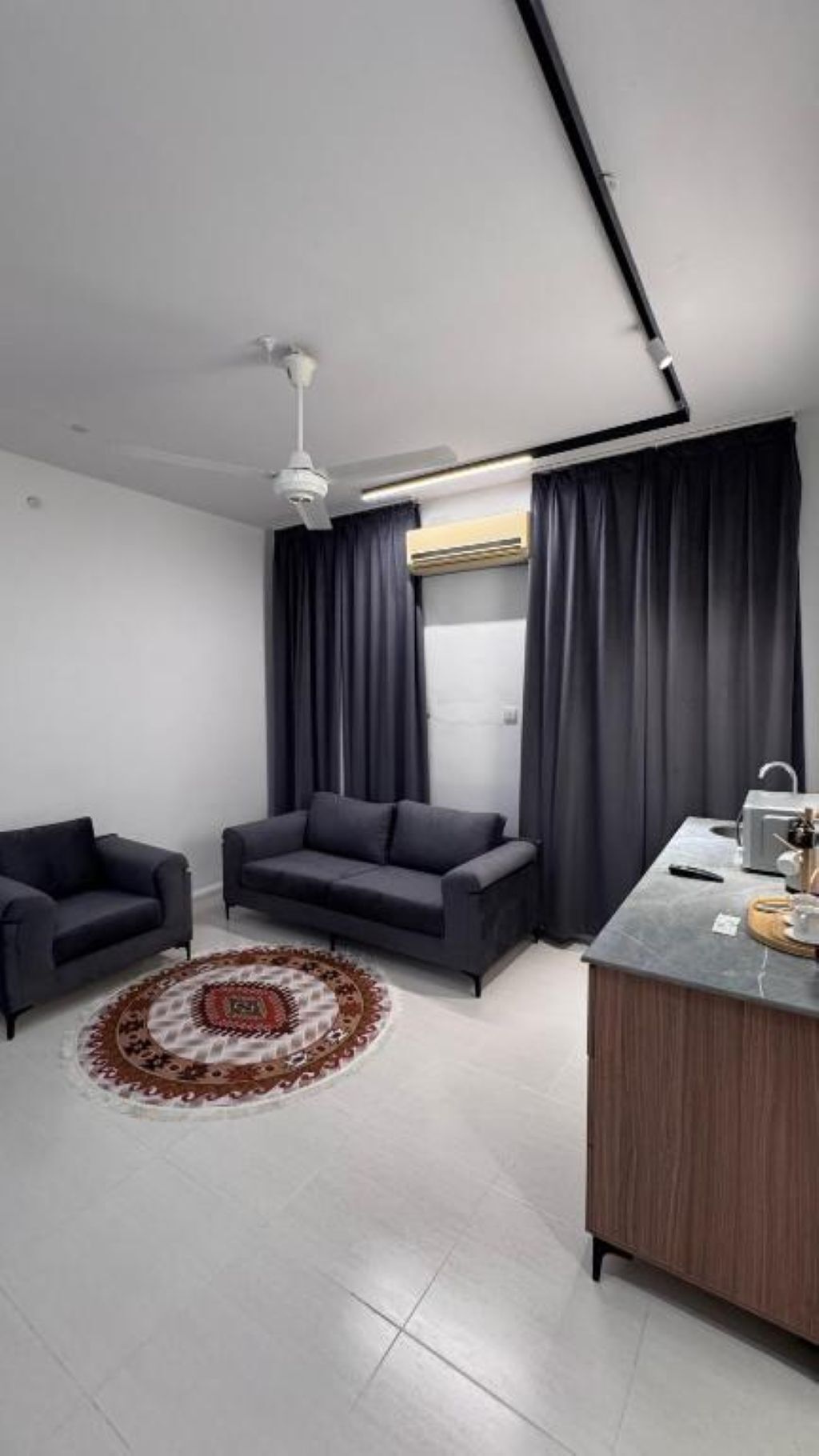 A modern living room with a sofa, two armchairs, a coffee table, a rug, and a kitchenette area.