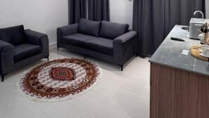 Una sala moderna con sofá, dos sillones, una mesa de centro, alfombra y una zona de kitchenette.