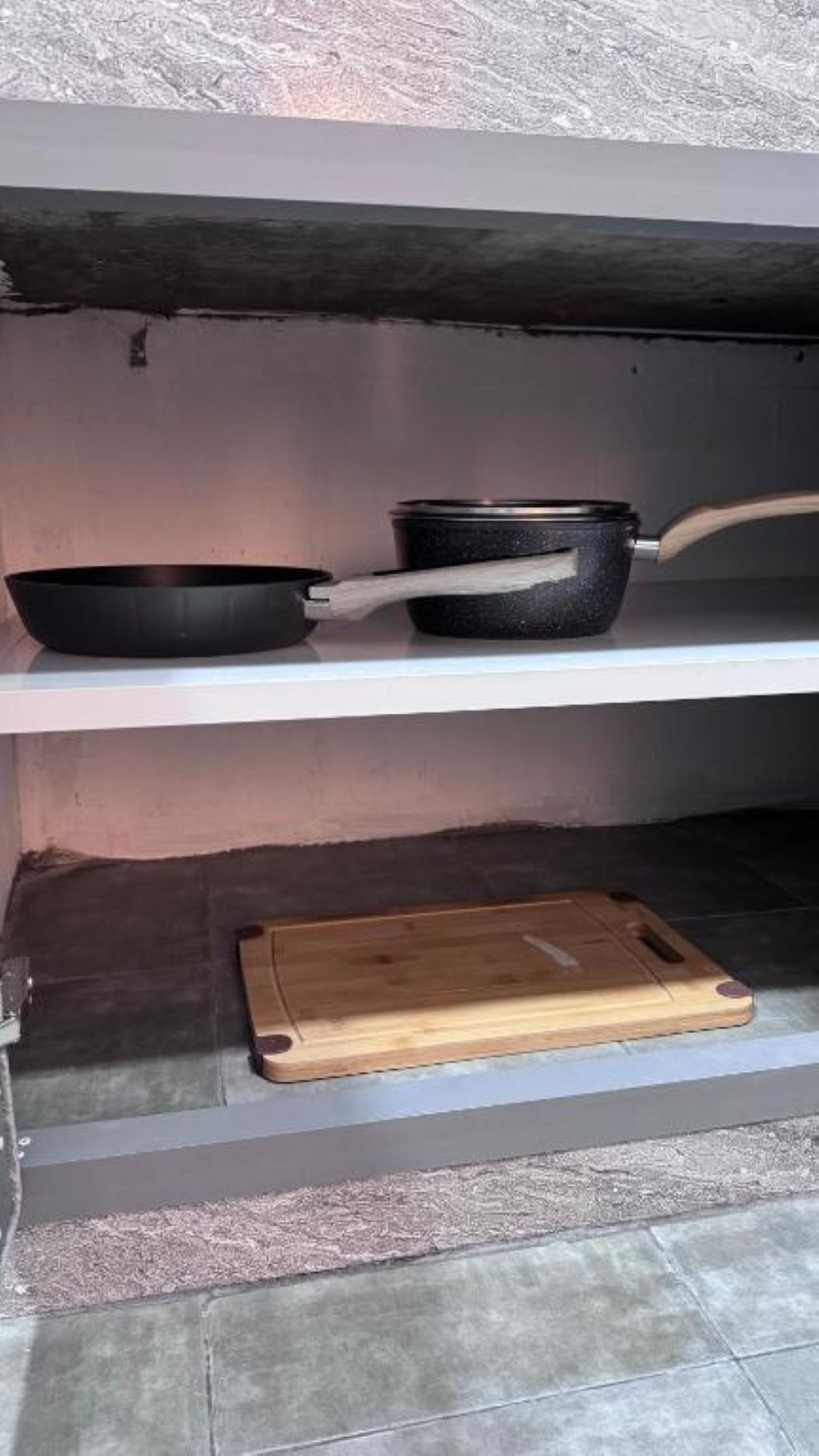 Un estante de cocina con una sartén, una olla y una tabla de cortar de madera.