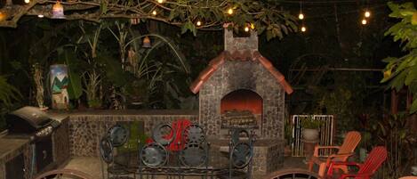 An outdoor patio with a stone fireplace, metal chairs, and a barbecue grill.