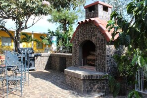 Un patio al aire libre con horno de piedra, sillas metálicas y plantas en macetas.