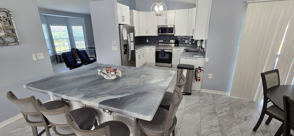 A modern kitchen with white cabinets, a stainless steel refrigerator, a microwave, an oven, and a sink.