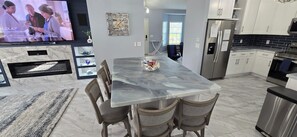 A modern kitchen with a marble countertop, stainless steel appliances, and a dining area with a glass table and chairs.