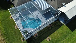 An aerial view of a swimming pool with a glass enclosure, surrounded by grass and a building.
