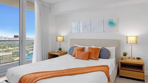 Ein Hotelzimmer mit einem großen Bett, zwei Nachttischen, Blick auf die Stadt und Bildern an der Wand.