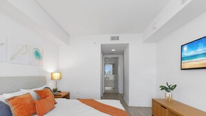 Quarto de hotel com cama, mesa de cabeceira, luminária, televisão e vista para a praia.