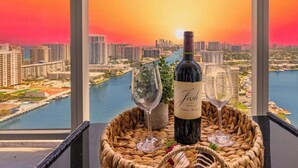 Uma varanda com vista para a paisagem urbana e um rio, uma garrafa de vinho, duas taças de vinho e uma cesta com lanches.
