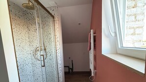 Een smalle gang met een douchecabine van glas en een raam met een bakstenen muur buiten.