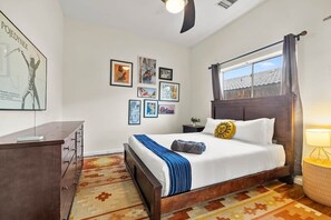 Un dormitorio con cama, cómoda, ventana con cortinas y obra de arte en la pared.