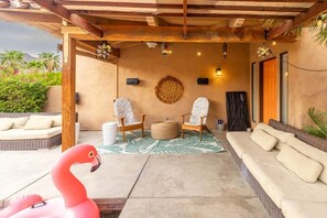 Ein überdachter Außenbereich mit zwei Stühlen, einem Sofa und einer Flamingo-Dekoration.
