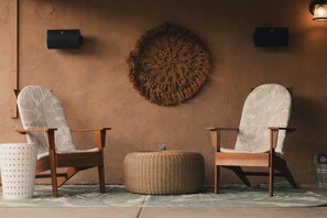 A room with two wooden chairs with white cushions, a woven ottoman, and a textured wall hanging. - Welcome to the Hotel California in the Historic La Quinta Cove (La Quinta)