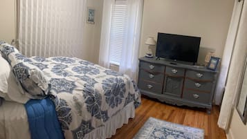 A bedroom with a bed, a dresser, a television, and a window with curtains.