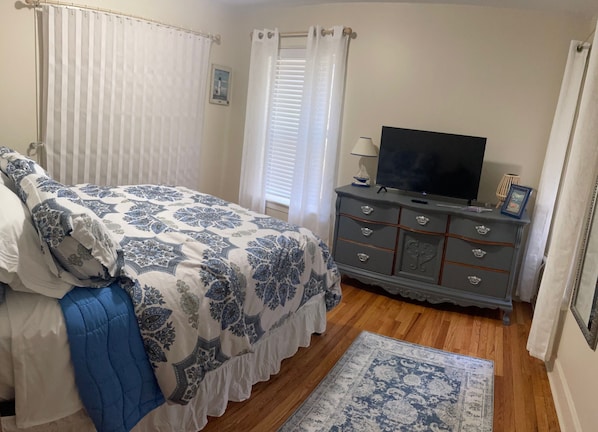 Un dormitorio con cama, cómoda, televisor y ventana con cortinas.