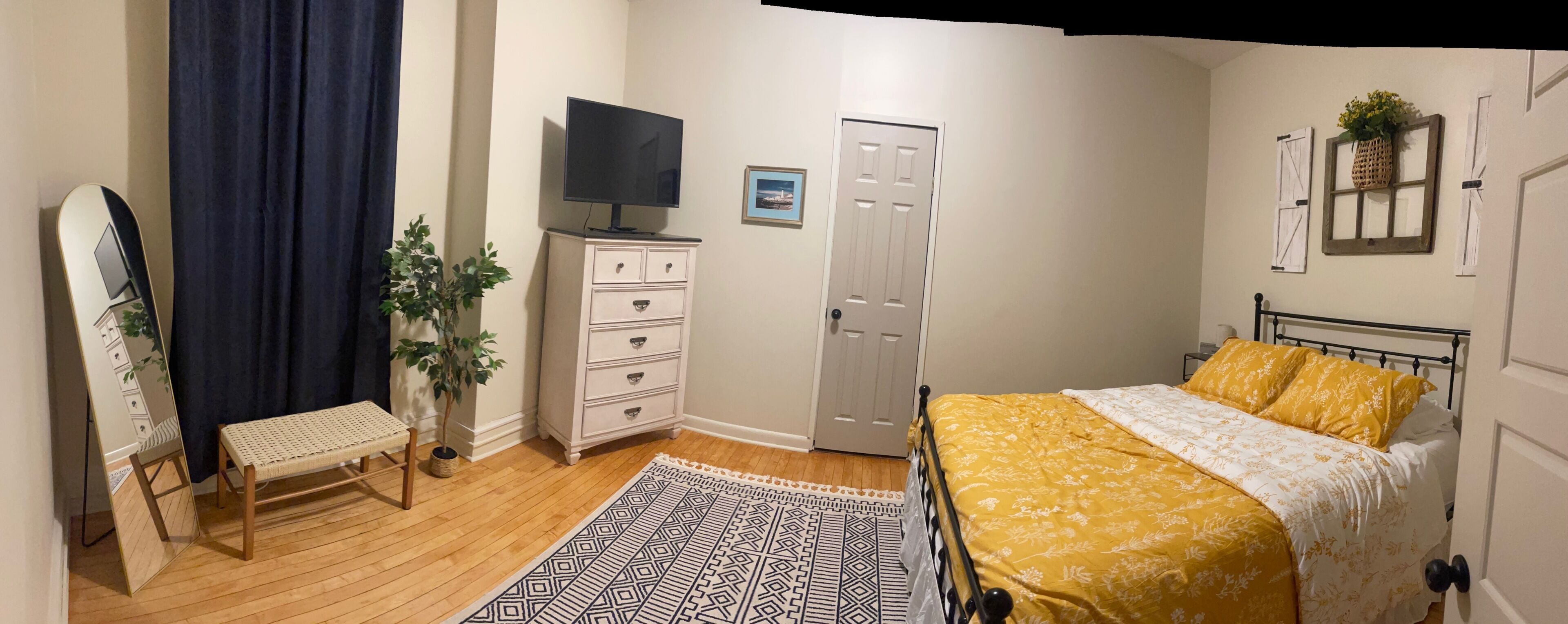 A bedroom with a bed, a dresser, a television, a door, and a window with curtains.