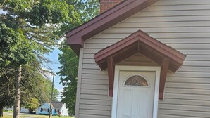 Un edificio residenziale con una porta bianca, un piccolo portico e un bidone dei rifiuti.