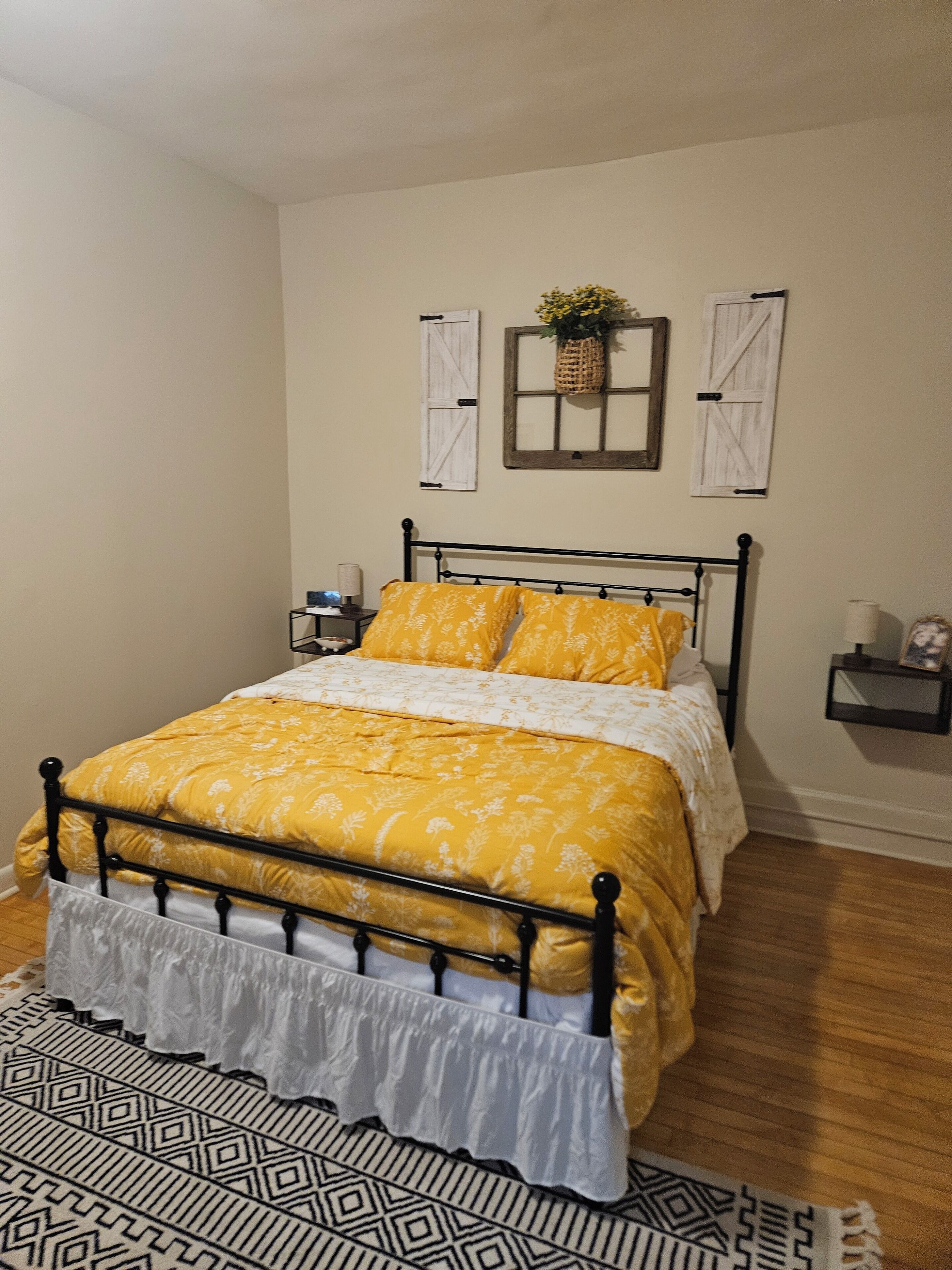 Quarto com cama, mesa de cabeceira, tapete estampado e prateleira na parede.