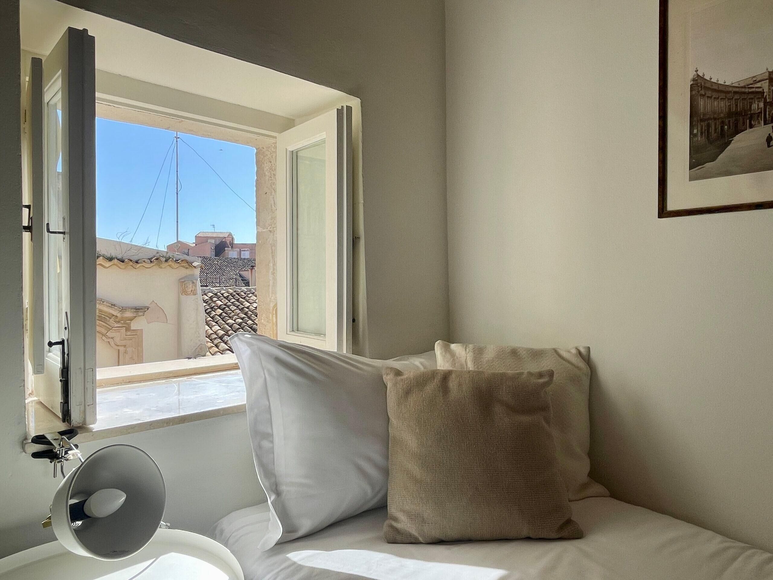 Una camera da letto con un letto, cuscini, una lampada da comodino e una finestra vista edifici.