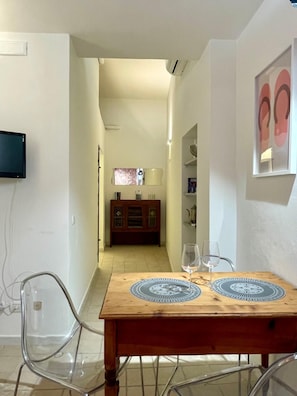Ein Essbereich mit einem Holztisch, transparenten Stühlen und einem an der Wand befestigten Fernseher.