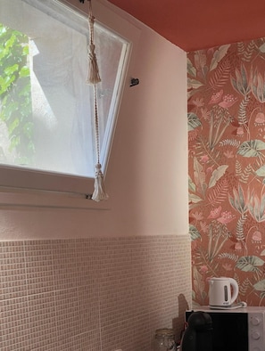Eine Küche mit Fenster, einer Pendelleuchte, einer Mikrowelle und einem Wasserkocher auf der Arbeitsplatte.