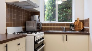 A kitchen with a gas stove, microwave, and a window with a view of greenery. - The Courtyard on Buckley (Moonee Ponds)